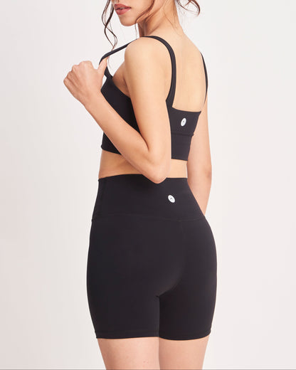 Woman wearing a black sports bra and high-waisted shorts on a white background