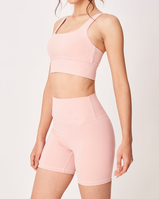 Person wearing a pink sports bra and shorts set on a light background