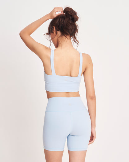 Person wearing a light blue sports bra and shorts set on a white background